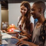 Two travelers check in at a hotel reception, smiling and engaging with the staff.